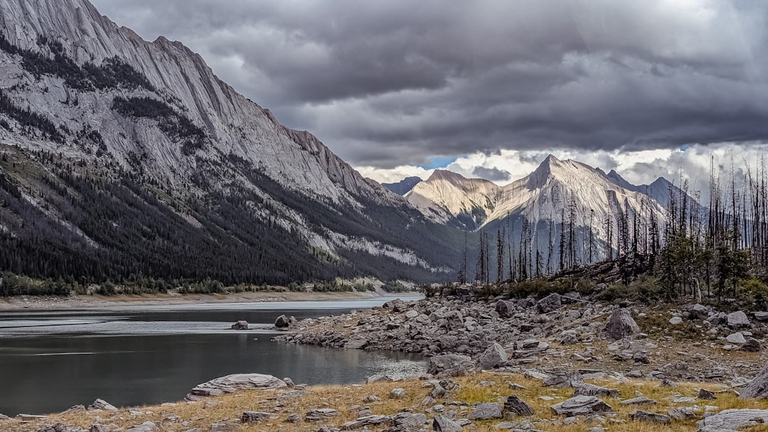 Dramatic mountains rise above a rocky lake shore.