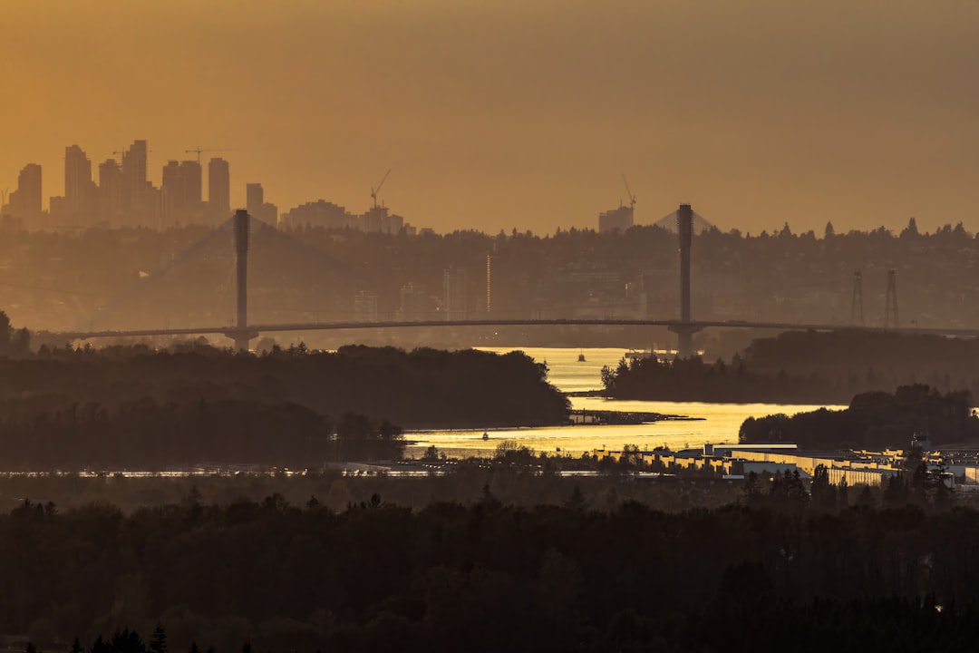 Golden sunset over a bridge, water, and distant city skyline.