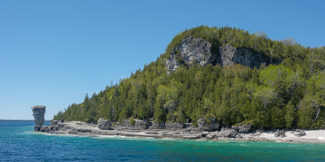 Unique rock formation, forested cliff, and clear blue water.